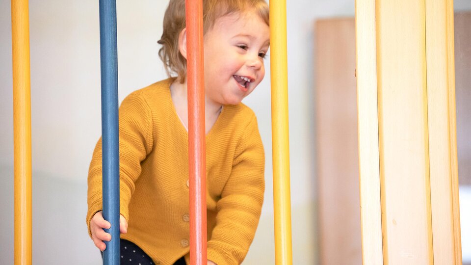 A cheerful child is playing on a playground device. They are wearing a yellow sweater and smiling happily.