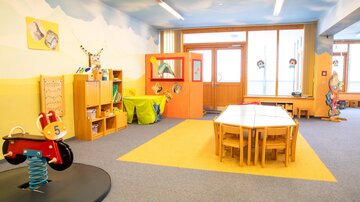 A bright and cheerful kindergarten room with colorful furniture. There are toys, tables, and lots of space to play.