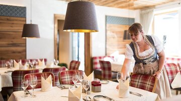 Ein gemütliches Restaurant mit einem einladenden Ambiente. Eine Kellnerin deckt den Tisch mit eleganten Gläsern und Servietten.