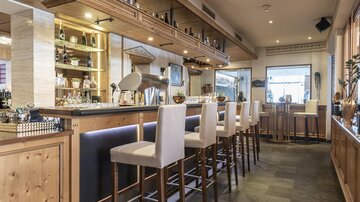 An elegant bar area with wooden paneling and modern bar stools. The space is well-lit and offers an inviting atmosphere.
