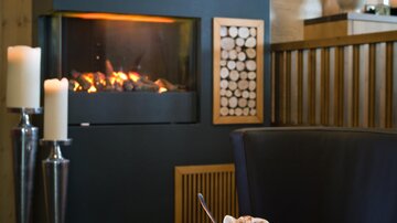 A cozy living space with a modern fireplace and candlelight. On the table, there is a drink and a book that create a relaxed atmosphere.