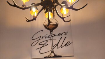 A stylish light object made of antlers hangs above an elegant wall mural. The image features the inscription "Grisoeners Edle".