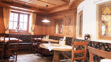 Ein gemütliches Restaurant mit Holzvertäfelung und traditionellen Tischen. Die Einrichtung ist rustikal mit bequemen Bänken und Fenster mit bunten Gläsern.