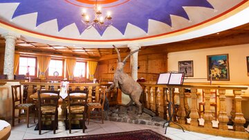 Ein gemütliches Restaurant mit rustikalem Dekor und einem bunten Deckenmuster. Eine Statue eines Bergtieres steht prominent im Raum.