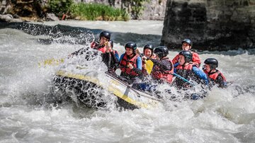 Eine aufregende Raftingtour auf wildem Wasser mit mehreren Personen im Boot. Alle tragen Helme und Schwimmwesten.