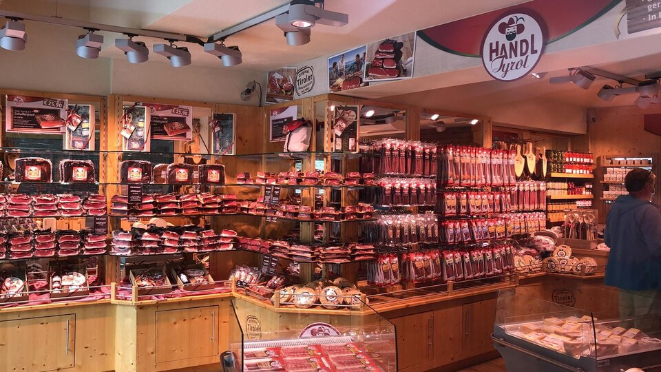 Ein Metzgergeschäft mit vielen Fleischprodukten und Holzregalen. Die Wände sind mit verschiedenen Wurstsorten dekoriert.