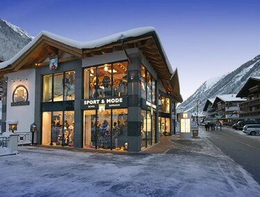 A modern shop in the Alps, surrounded by snow-capped mountains. The facade is extensively glazed and inviting.