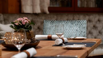 Ein eleganter Tisch mit schönem Geschirr und Gläsern, dekoriert mit einer kleinen blühenden Pflanze. Die Umgebung wirkt gemütlich und einladend.