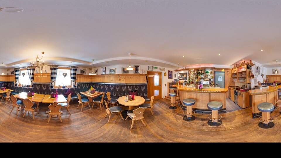 A cozy bar with wooden furniture and tables. The walls are decorated and there is a well-equipped bar in the background.