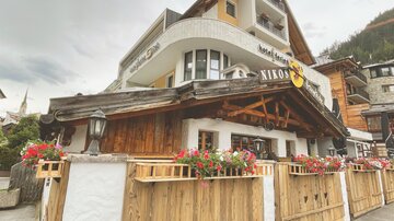 Ein charmantes Hotel mit holzverkleideter Fassade und bunten Blumen. Im Hintergrund sind traditionelle alpine Gebäude sichtbar.