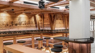 Ein gemütlicher Innenraum mit Holzwänden und einer modernen Bar. Es gibt hohe Sitzplätze und eine angenehme Beleuchtung.