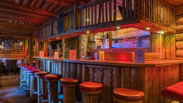Eine gemütliche Holzbar mit bunten Lichtern und runden Hockern. Die Atmosphäre ist warm und einladend.