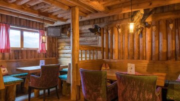 Ein gemütliches Restaurant mit Holzwänden und rustikalem Design. Die Sitzplätze sind mit bunten Stoffen ausgestattet und es gibt Fenster mit Blick nach draußen.