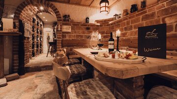 Eine gemütliche Weinstube mit Holztisch und dekadentem Essen. Die Wände aus Ziegelstein und sanfte Beleuchtung schaffen eine einladende Atmosphäre.