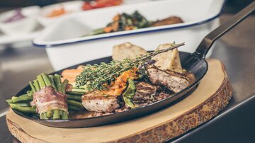 A delicious dish on an iron pan, combining tender meat with fresh vegetables. Spicy herbs and a refreshing sauce are served alongside.