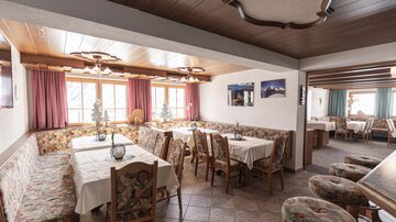 A cozy restaurant with paneled wooden walls and floral-patterned tables. The windows let in plenty of daylight, creating an inviting atmosphere.