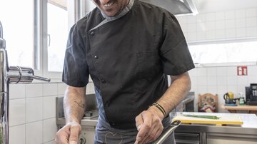 A chef is preparing a meal in a modern kitchen. Fresh ingredients are visible on the countertop.