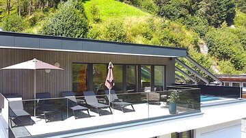 A modern terrace with loungers and a sun umbrella. Green hills can be seen in the background.