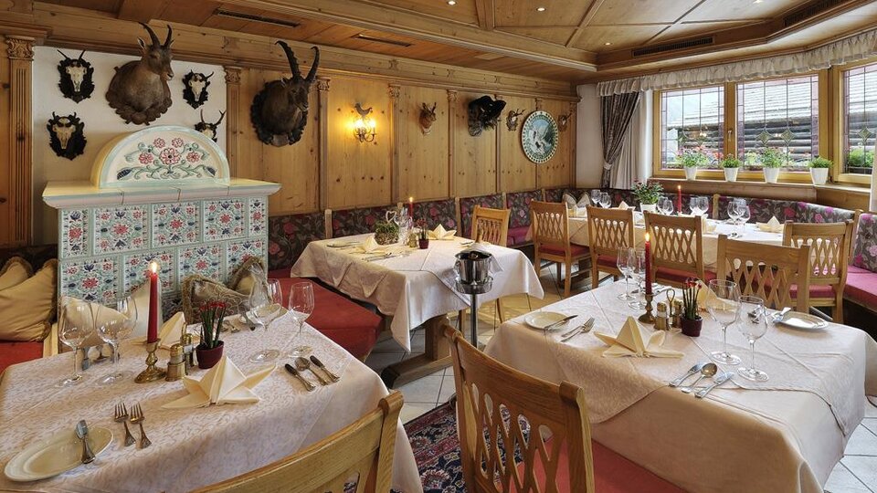 Ein gemütliches Restaurant mit Holzwänden und eleganten Tischdeckchen. Die Tische sind festlich gedeckt und die Dekoration umfasst traditionelle Jagdtrophäen.