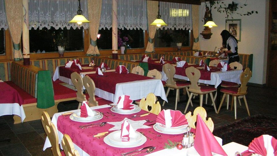 Ein einladendes Restaurant mit eleganten Tischen, die mit rotem Tischdecken und dekorativen Servietten gedeckt sind. Im Hintergrund ist eine Mitarbeiterin zu sehen, die den Service vorbereitet.