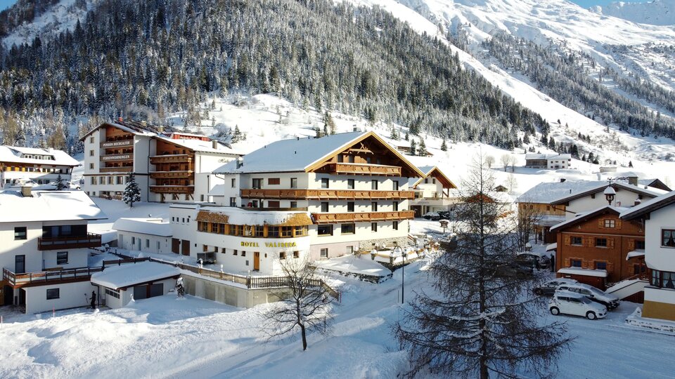Eine malerische Winterlandschaft mit verschneiten Häusern und Bergen im Hintergrund. Die Szene strahlt Ruhe und Gemütlichkeit aus.