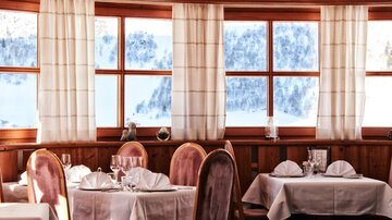 Ein gemütliches Restaurant mit eleganten Tischen und Stühlen. Große Fenster bieten einen Blick auf eine verschneite Landschaft.