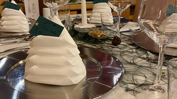 Ein festlich gedeckter Tisch mit elegant gefalteten Servietten in Form eines Berges. Gläser und Silberbesteck runden die festliche Atmosphäre ab.