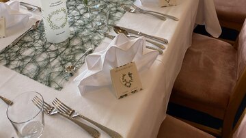 Ein elegant gedeckter Tisch mit weißen Tischdecken und dekorativen Servietten. In der Mitte befinden sich Kerzen und Blumen, die eine festliche Atmosphäre schaffen.