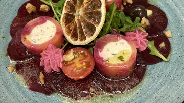 Ein kunstvoll angerichteter Teller mit roter Beete, frischem Rucola und gefüllten Röllchen. Das Gericht ist dekoriert mit getrockneter Zitrone und bunten Garnituren.