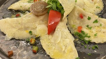 Ein köstlicher Teller mit gefüllten Teigtaschen, garniert mit Frischkäse und frischem Gemüse. Die Speise liegt auf einem dunklen Teller und ist ansprechend angerichtet.