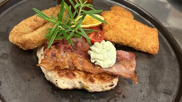 Ein leckeres Gericht mit gebratenem Fleisch, Beilage und einer Sauce. Frische Kräuter und ein Stück Zitrone garnieren die Präsentation.