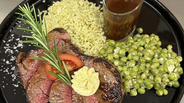 Ein Gericht mit saftigem Steak, kombiniert mit grünem Reis und Erbsen. Dazu gibt es eine Sauce in einem Glas und frische Kräuter.