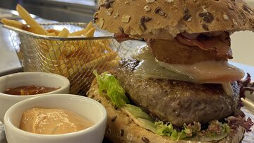 Ein saftiger Burger aus Vollkornbrot mit Salat, Speck und einer Scheibe Ananas. Dazu gibt es Pommes und zwei verschiedene Dips.
