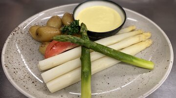 Ein Teller mit weißem Spargel, grünen Spargel und kleinen Kartoffeln. Dazu gibt es eine Schüssel mit Sauce.