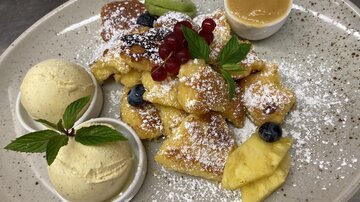 Ein Teller mit köstlichen Krapfen, garniert mit frischen Beeren und Minze. Dazu gibt es zwei Kugeln Eis und eine Schale Karamellsauce.