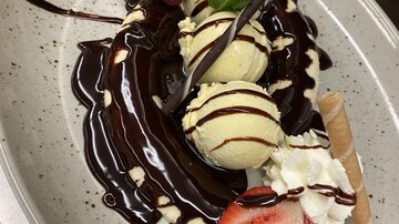 Ein köstliches Dessert mit Vanilleeis, Schokoladensoße, frischen Erdbeeren und Sahne. Garniert mit Minze und Waffelhörnchen.