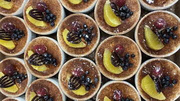 Eine Anordnung von Dessertschalen mit einer goldbraunen Oberfläche. Die Desserts sind mit Früchten wie Himbeeren, Heidelbeeren und Zitronenscheiben garniert.