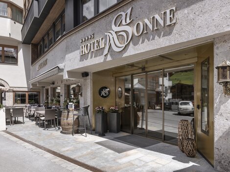 The entrance to the Hotel Sonne is stylishly designed and inviting. There are outdoor seating areas and a modern facade.