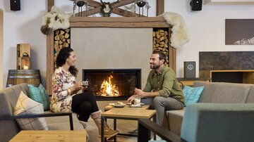 A cozy room with a fireplace and two people who are chatting. They are enjoying hot beverages and a relaxed atmosphere.