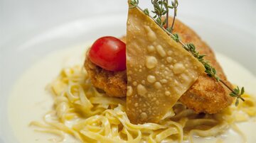 Ein leckeres Gericht mit knusprigem Hähnchen, serviert auf einem Bett von Nudeln in einer cremigen Soße. Gekrönt mit einer Tomate und einem knusprigen Chip.
