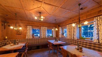 A cozy restaurant with wooden decor and warm lighting. The tables are neatly set and the window curtains create an inviting atmosphere.