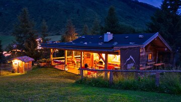 A cozy chalet in the mountains at twilight. The illuminated interior and the surrounding nature create an inviting atmosphere.