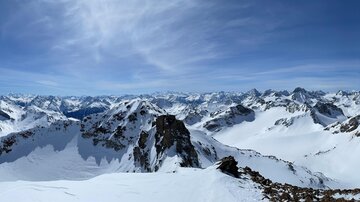 An impressive mountain landscape with snow-covered peaks and a clear blue sky. The view is vast and breathtaking.