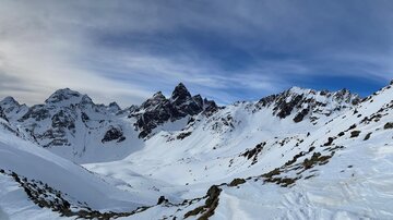 An impressive mountain landscape with snow-covered peaks and a blue sky. The sun shines over the wintry scene.