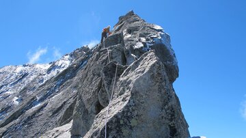 A steep rock under a clear blue sky. Rope and climbing gear suggest mountaineering.