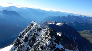 An impressive mountain landscape with snow-capped peaks and deep valleys. The clear sky makes the majestic beauty of the Alps shine.