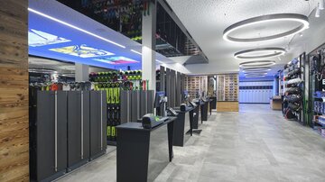Ein moderner Sportgeschäftsraum mit einer hellen Atmosphäre. Auf der linken Seite sind Skiausrüstungen und eine großzügige Kasse zu sehen.