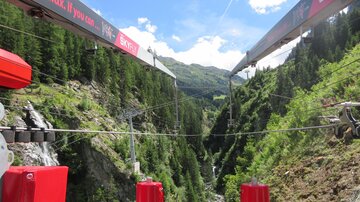 Eine Seilbahn mit Aussicht auf eine grüne Schlucht. Der Himmel ist blau mit einigen Wolken.