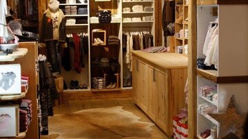 A beautiful fashion store with wooden furniture and a warm atmosphere. Shelves full of clothing and accessories invite you to browse.