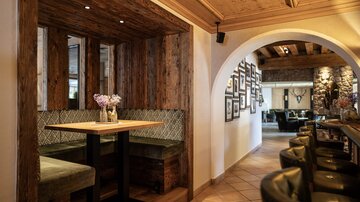 A cozy restaurant with wooden walls and elegant seating areas. In the background, picture frames can be seen on the wall, and there is an inviting atmosphere.